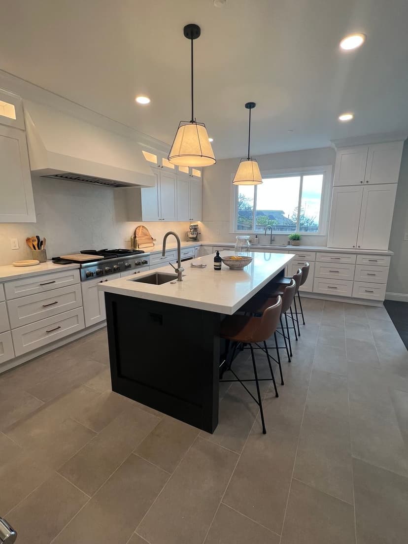 Modern kitchen with white cabinetry, black island, and stylish pendant lighting.