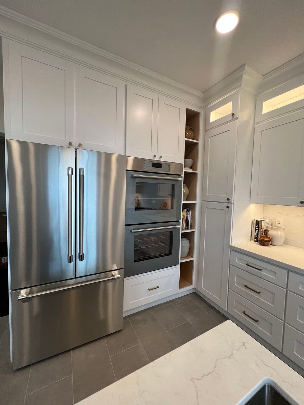 Modern kitchen featuring stainless steel refrigerator and built-in oven with white cabinetry.