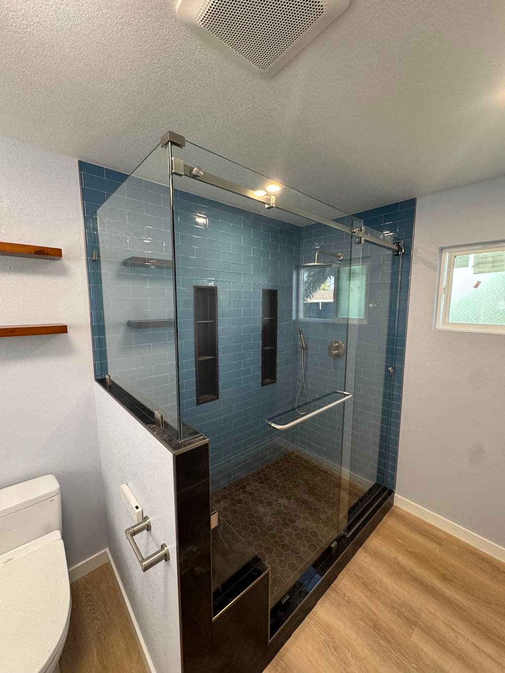 Modern shower enclosure with glass walls, blue tiles, and wood accents in a stylish bathroom.