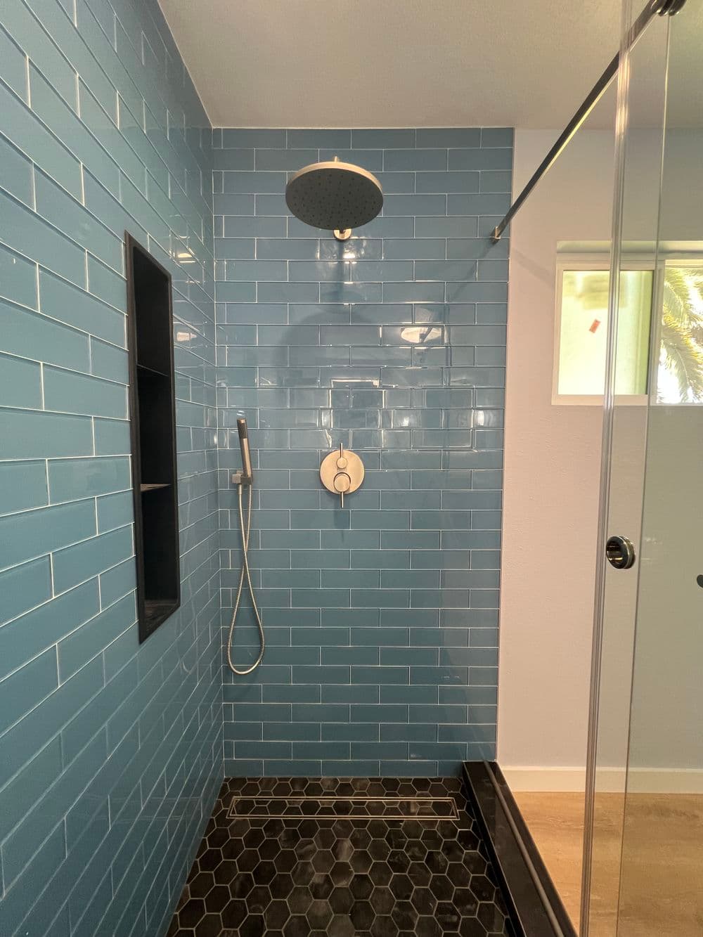 Modern shower with blue subway tiles, overhead rainfall showerhead, and black tiled floor.