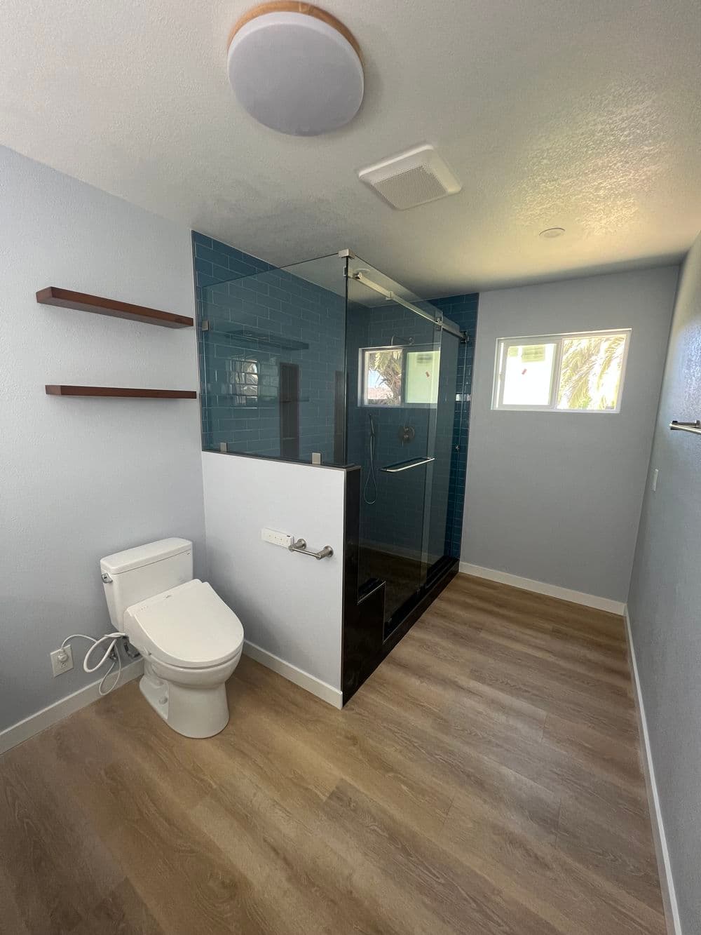Modern bathroom with glass shower, sleek toilet, and blue tile accents on walls.