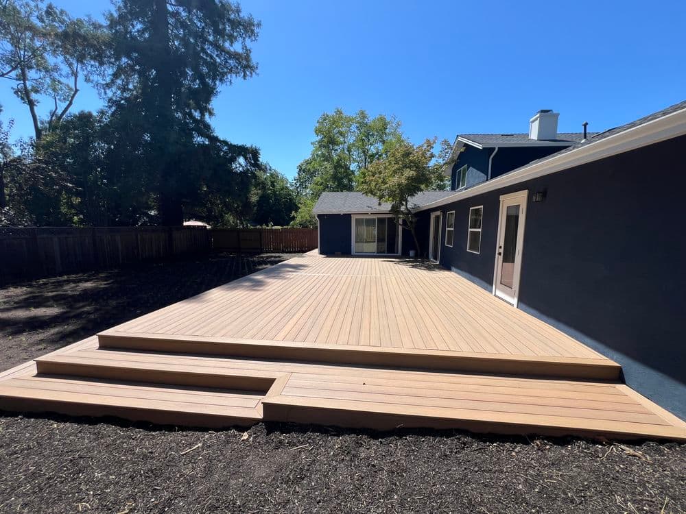Modern deck with stairs in backyard, surrounded by trees and blue sky. Ideal for outdoor living.