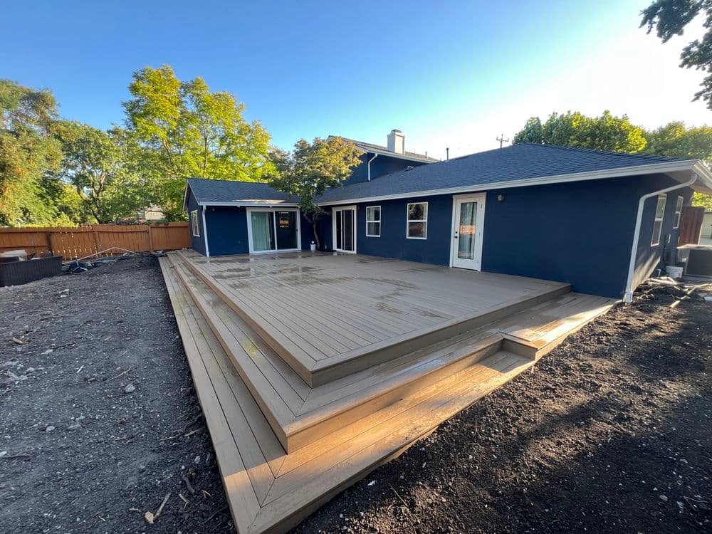 Modern home exterior with a spacious wood deck and landscaped yard on a sunny day.