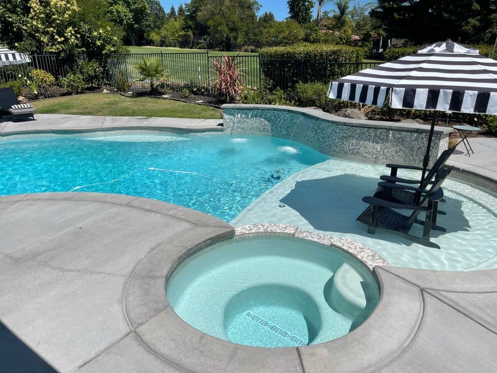 luxurious backyard pool with spa, black and white striped umbrella, lush landscaping