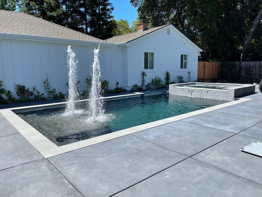 Modern backyard pool with fountains and spa surrounded by contemporary landscaping.