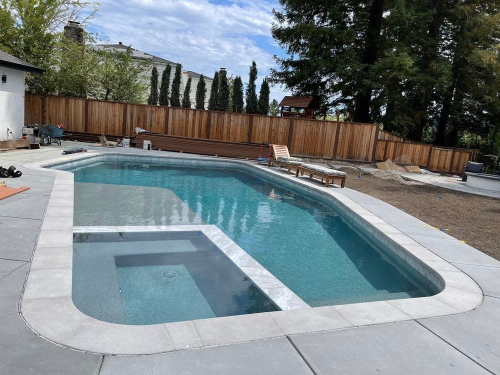 Modern backyard swimming pool with clear water, concrete decking, and wooden fencing.