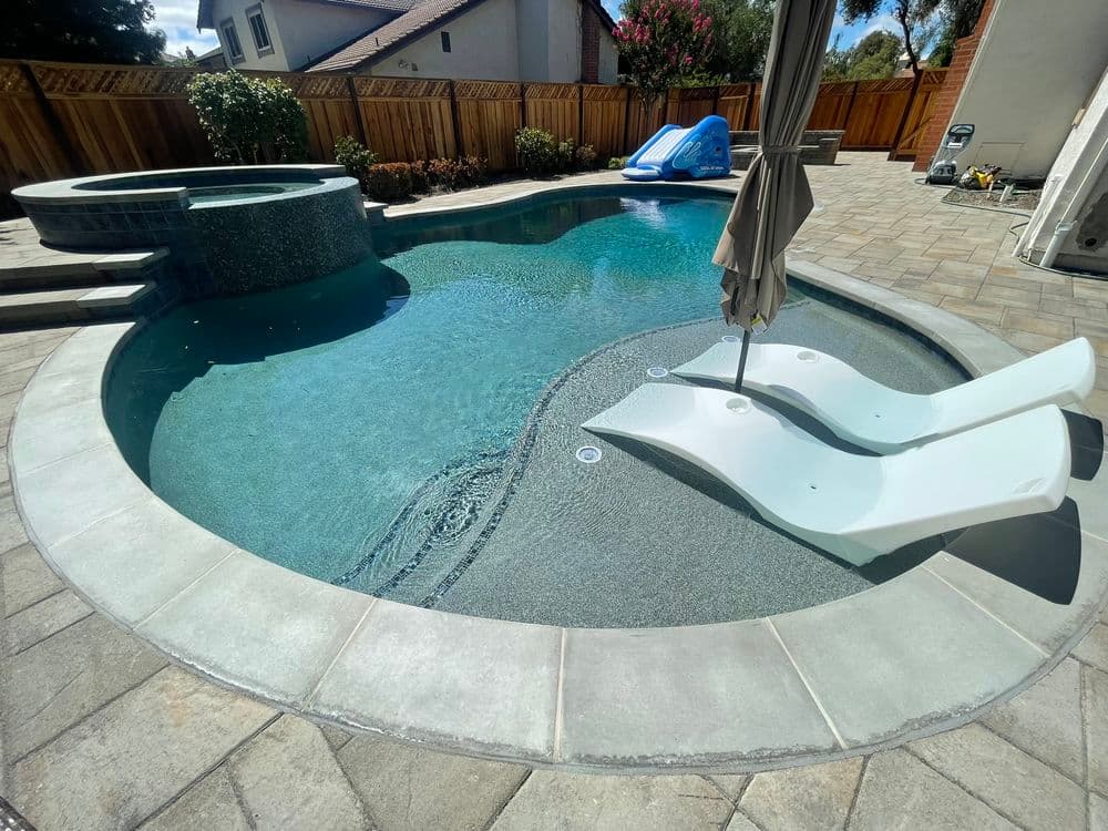 Luxury backyard pool with spa, loungers, and slide set in a sunny residential area.