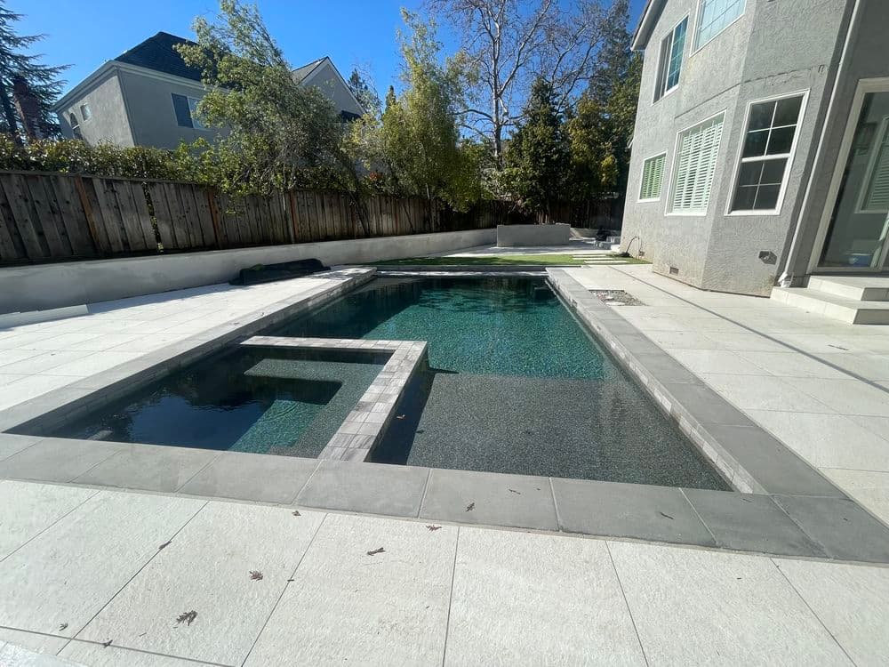 Modern backyard with a swimming pool, spa, and elegant stone patio in a sunny setting.