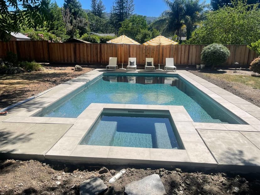 Modern backyard with a sparkling pool, spa, lounge chairs, and shaded areas under umbrellas.