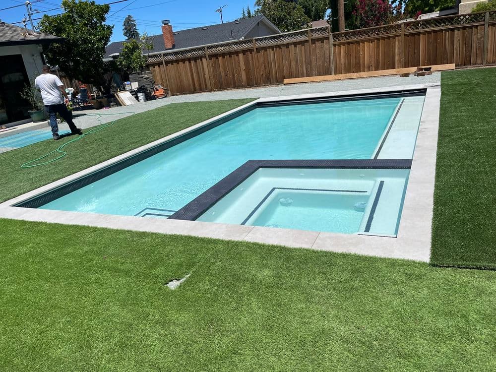 Modern rectangular swimming pool surrounded by artificial grass and a wooden fence.