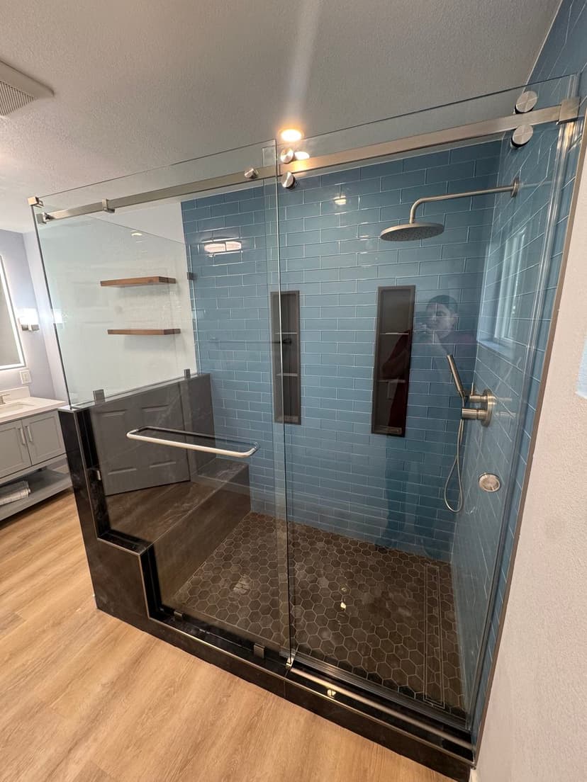 Modern glass shower with blue tiles, grab bars, and pebble floor in a stylish bathroom.