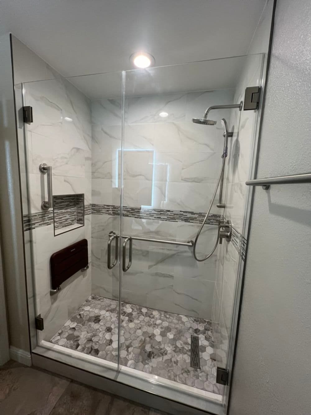 Modern glass shower enclosure with marble tiles and grab bars for accessibility.