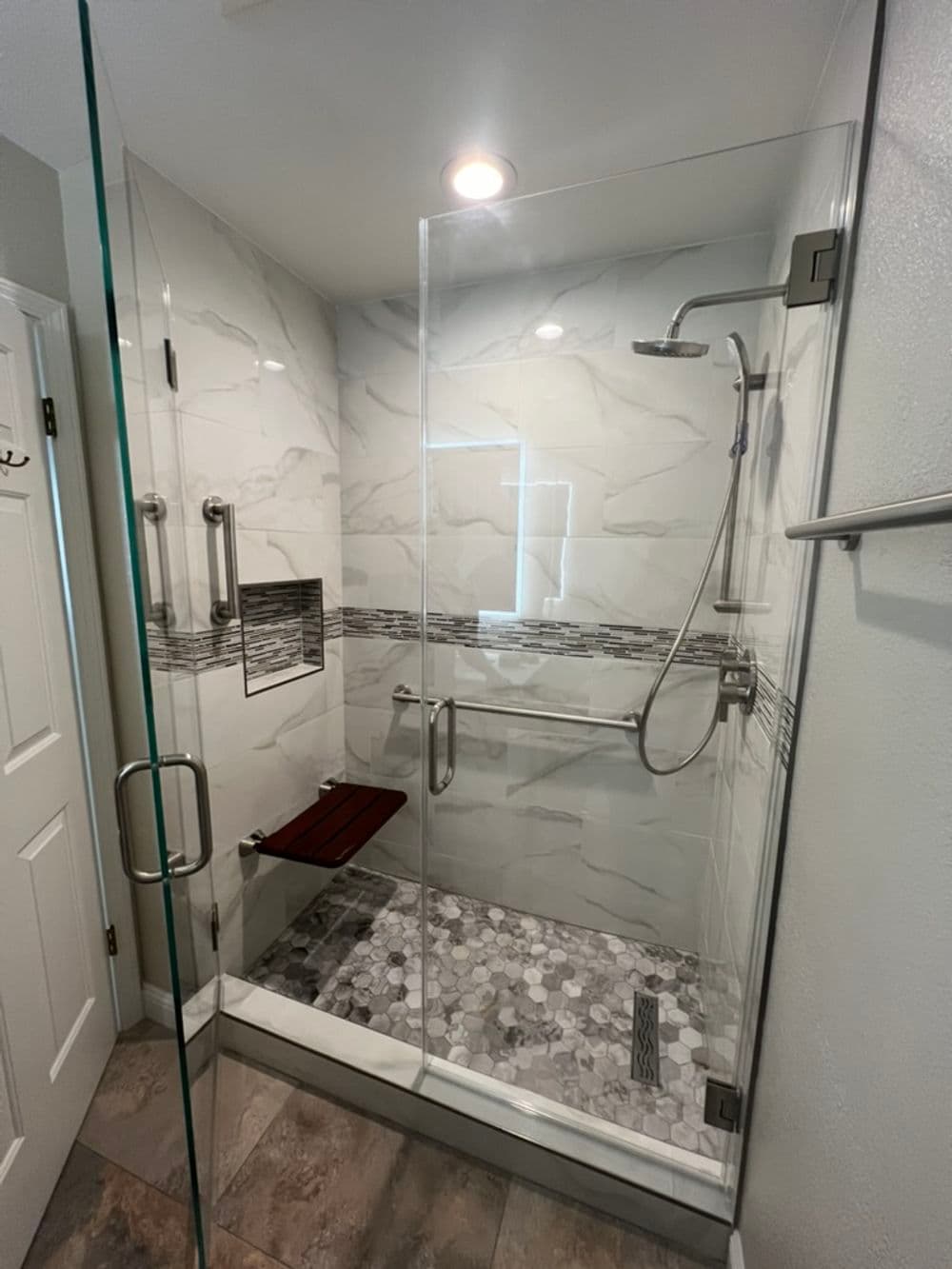 Modern walk-in shower with glass enclosure, marble accents, and grab bars for safety.