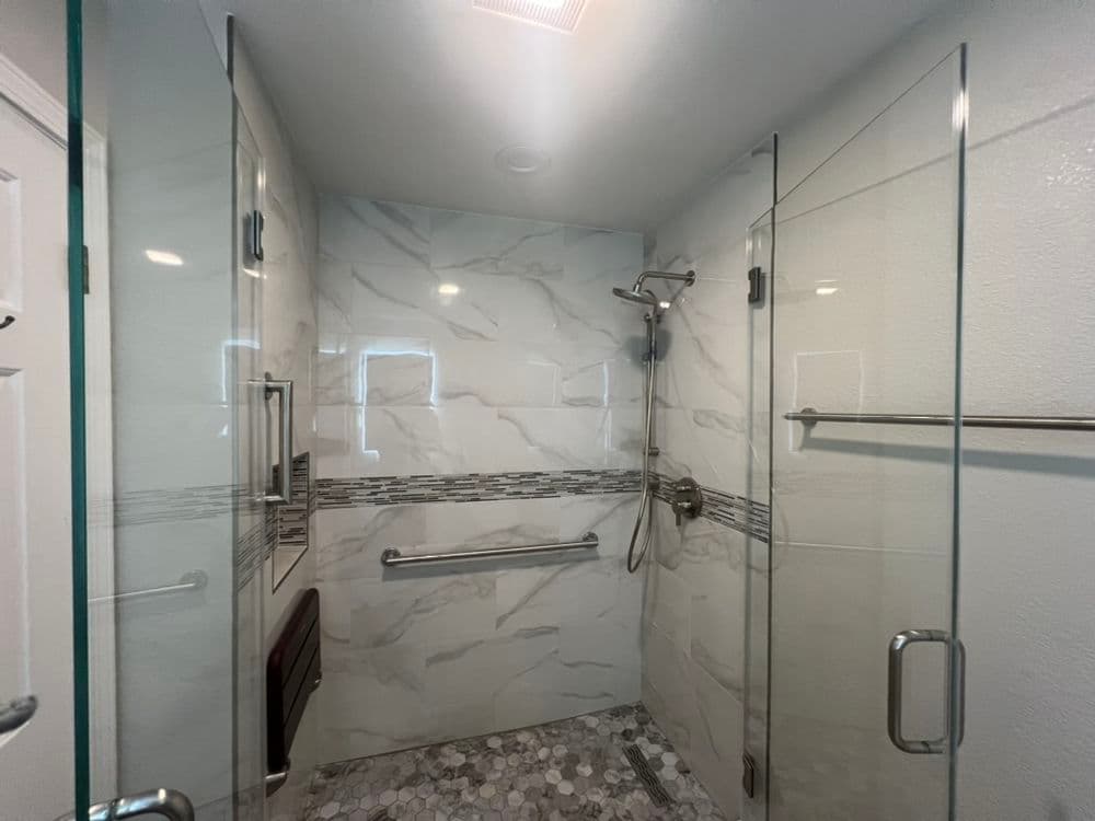 Modern walk-in shower with glass enclosures, marble walls, and safety grab bars.