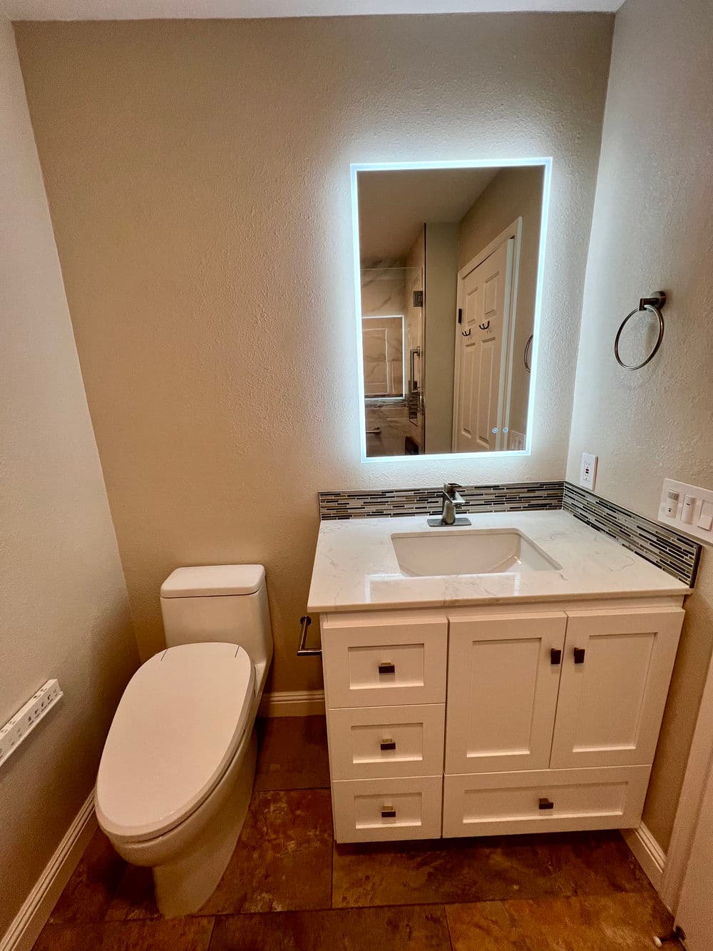 Modern bathroom with backlit mirror, white vanity, and sleek toilet design.