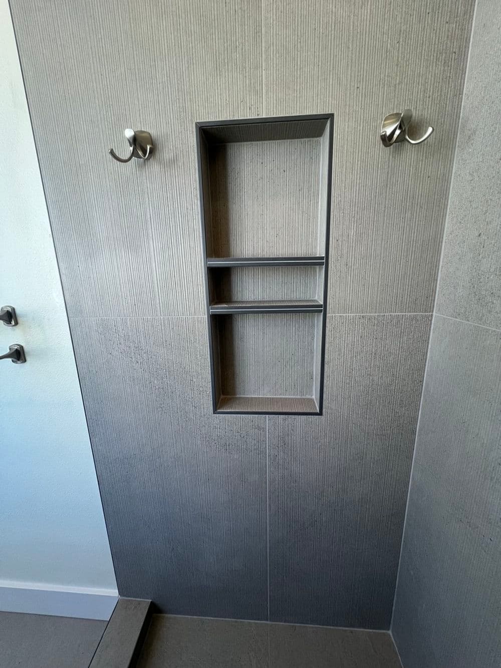 Modern shower with tiled walls, built-in shelf, and hooks for towels.