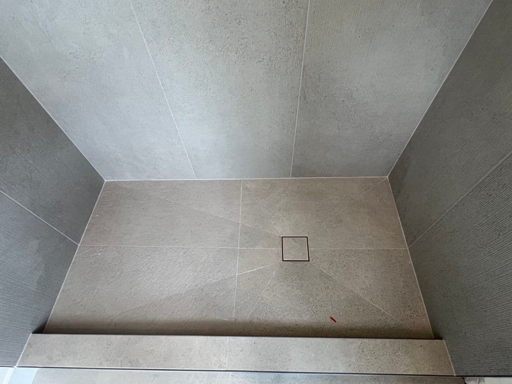 Modern gray tiled shower floor with a subtle drainage area in the center.