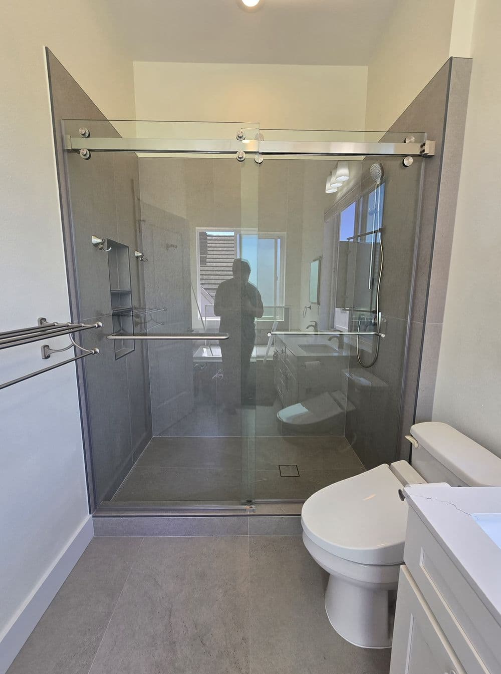 Modern bathroom with a glass shower, toilet, and stylish gray tiles. Natural light from window.