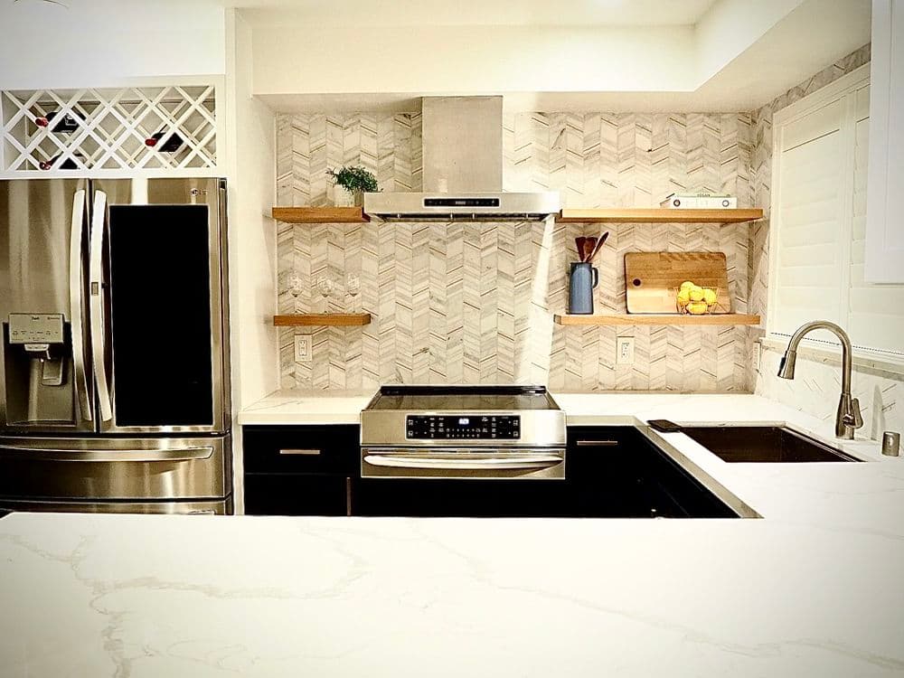 Modern kitchen featuring black cabinets, stainless steel appliances, and herringbone tile backsplash.