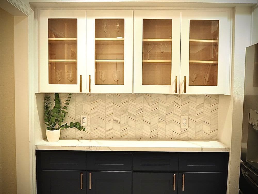 Modern kitchen cabinetry with glass doors, marble backsplash, and potted plant.