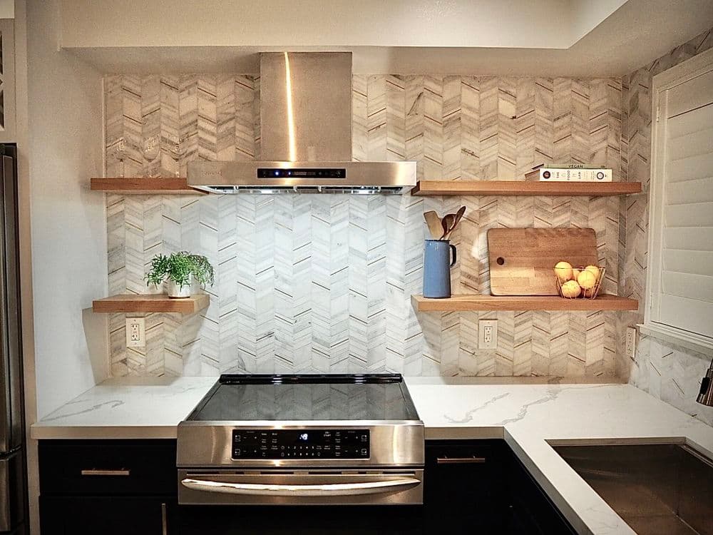 Modern kitchen featuring stainless steel range hood, herringbone backsplash, and wooden shelves.