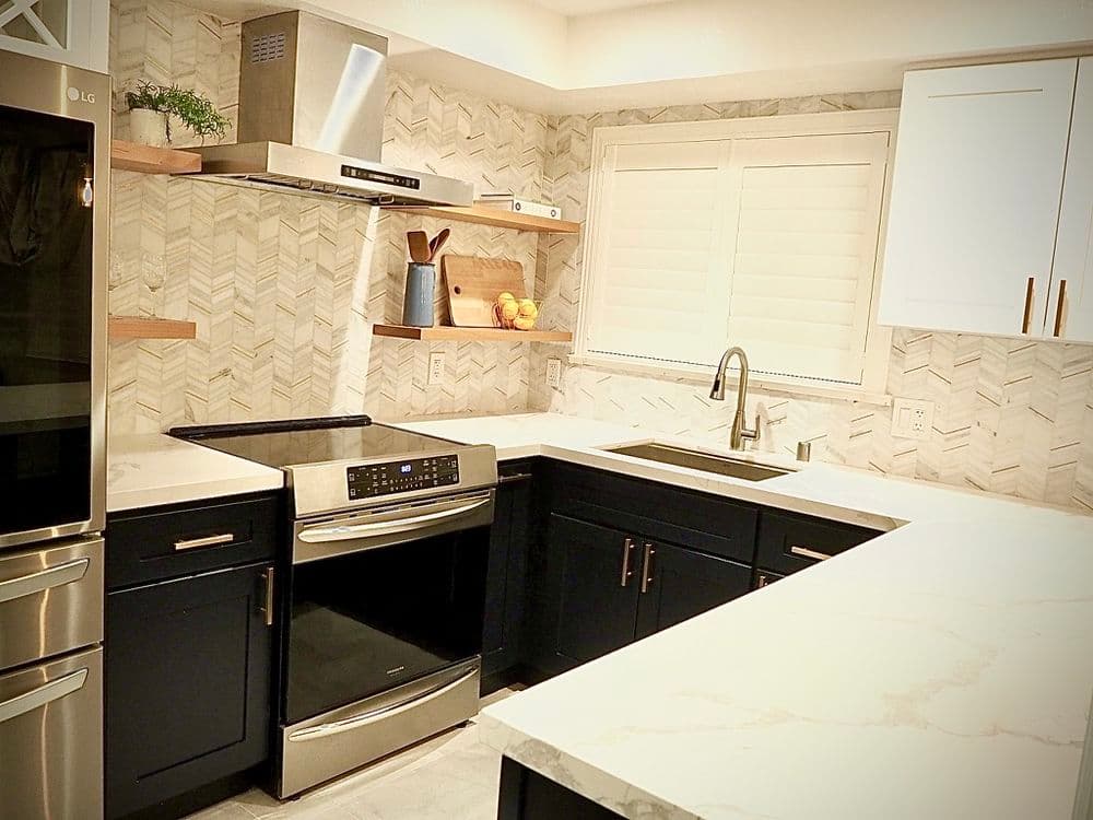 Modern kitchen with navy blue cabinets, marble countertops, and herringbone backsplash.