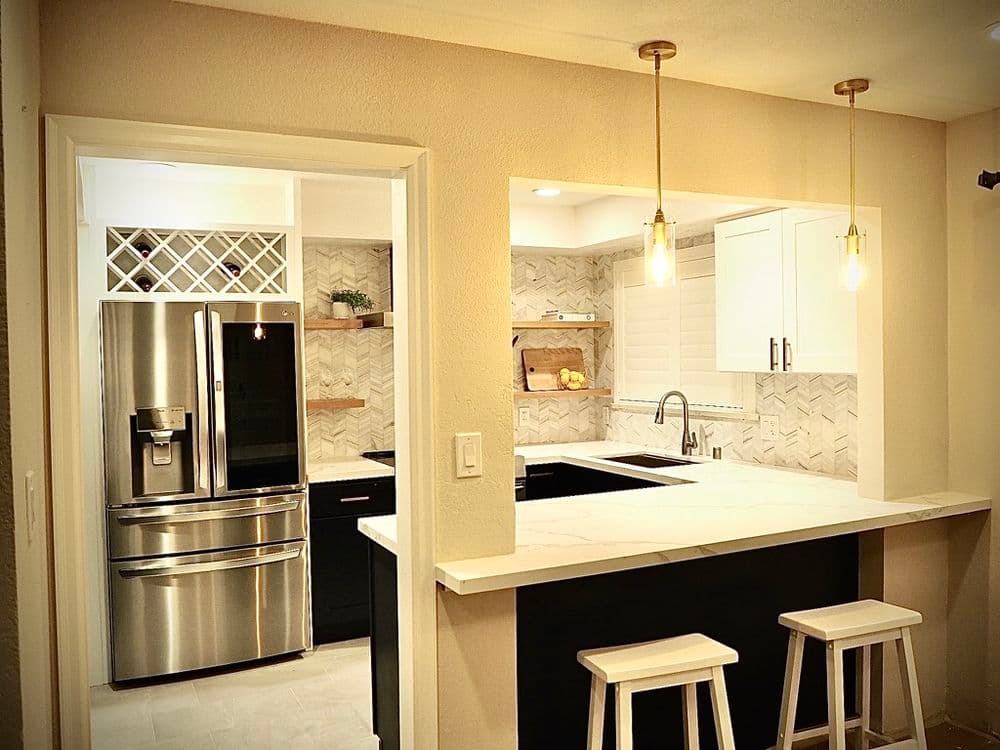 Modern kitchen with stainless steel appliances, white cabinets, and open bar area with stools.