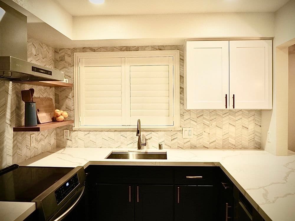 Modern kitchen with herringbone backsplash, black cabinets, and stainless steel appliances.