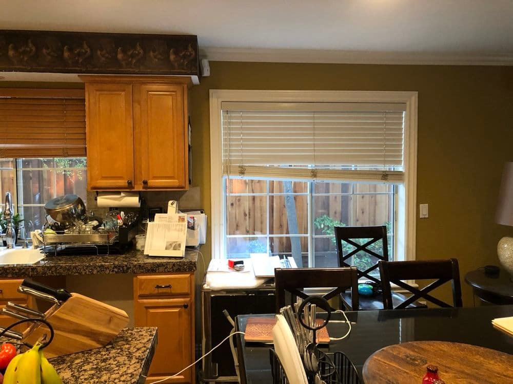 Warm kitchen interior with wooden cabinets, granite countertops, and sunlight filtering through blinds.
