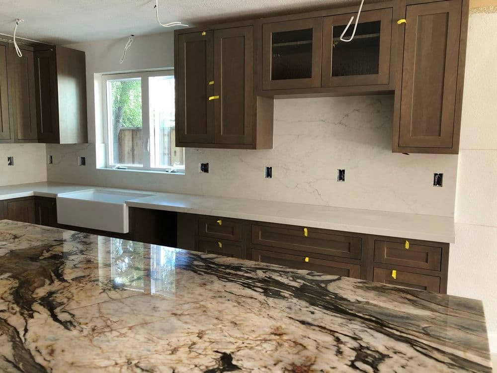 Modern kitchen with dark wood cabinets, marble countertop, and natural light from window.