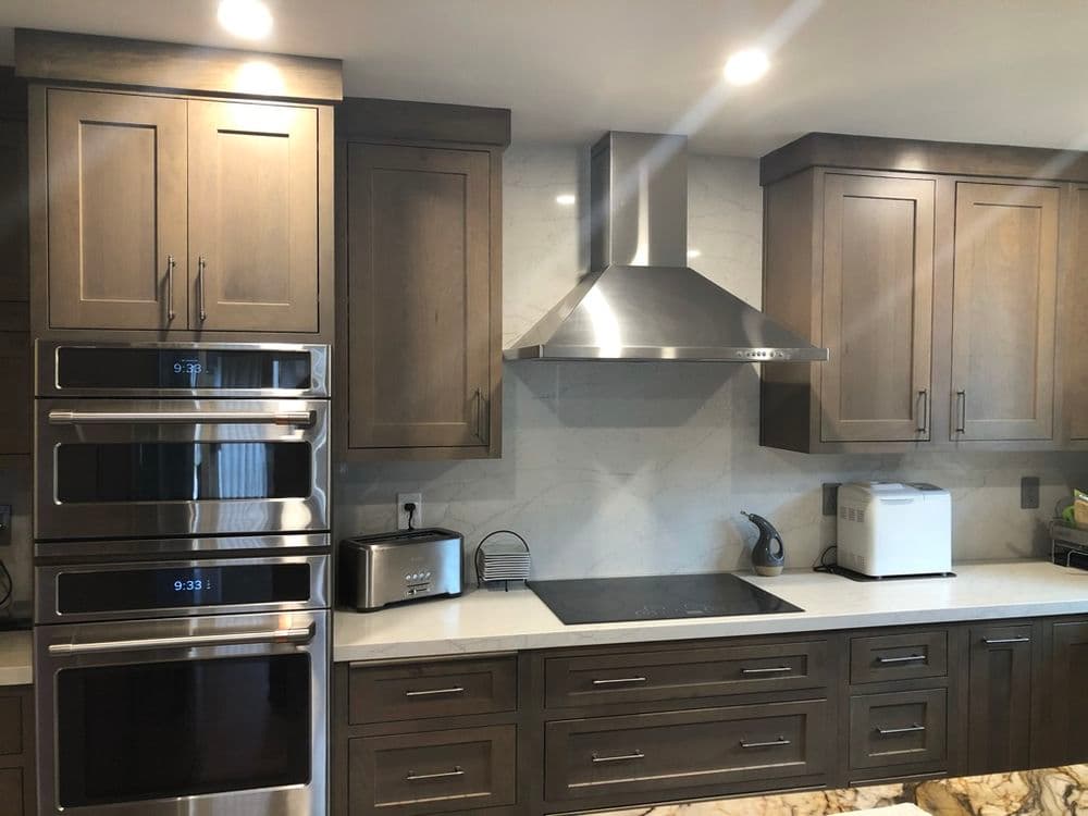 Modern kitchen with stainless steel appliances, wood cabinetry, and marble countertops.
