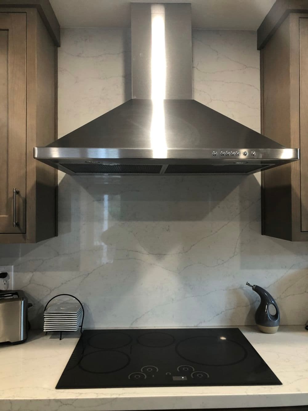 Modern kitchen with stainless steel range hood and glass stovetop against a marble backsplash.