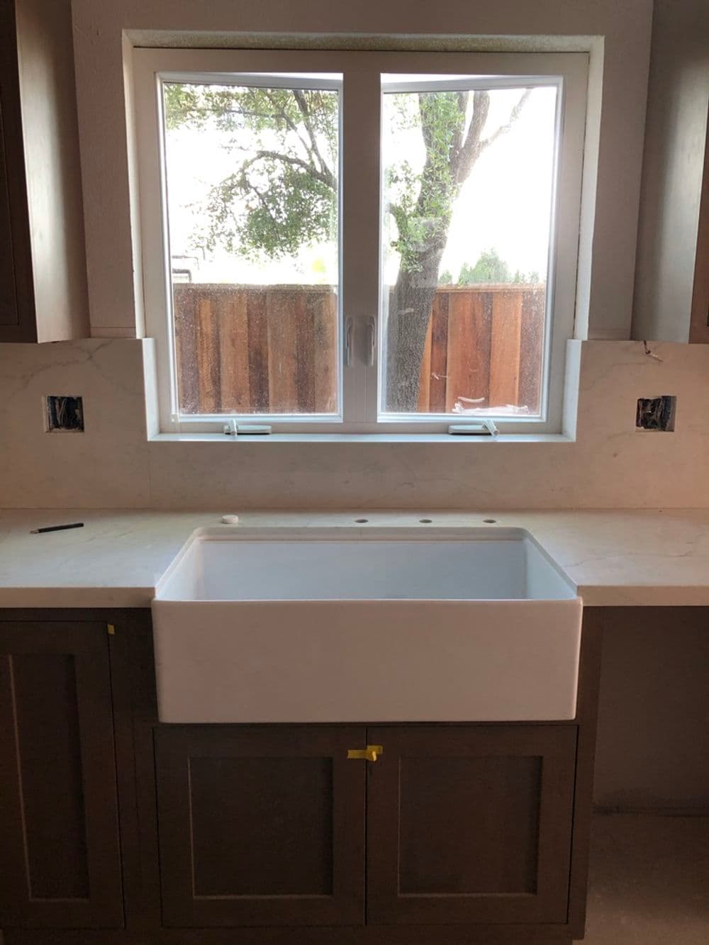 Farmhouse sink installed in a modern kitchen with a view of a tree outside through a window.