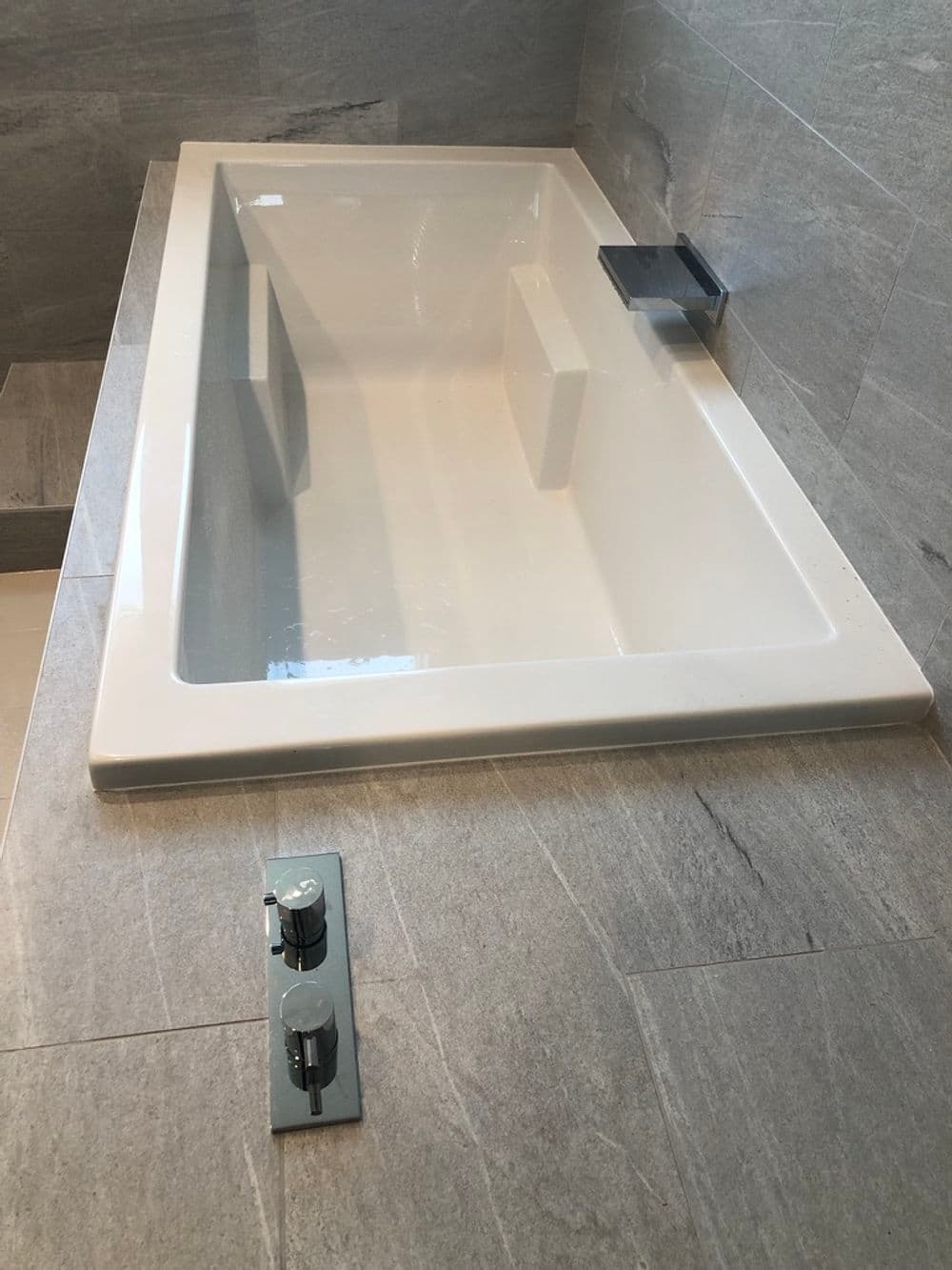 Modern freestanding bathtub with sleek faucet on textured gray tile floor.