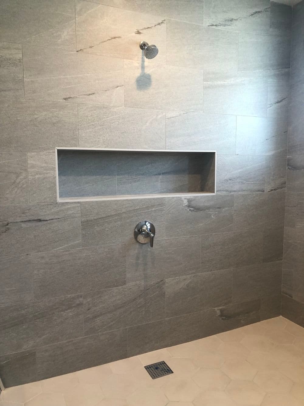 Modern shower with gray tiled walls, niche for toiletries, and sleek faucet design.