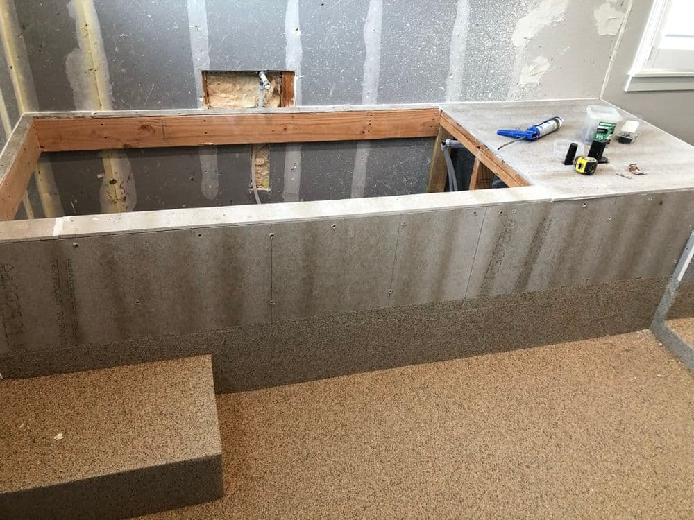 Bathroom renovation showing a partially built bench with cement board and tools in a modern setting.