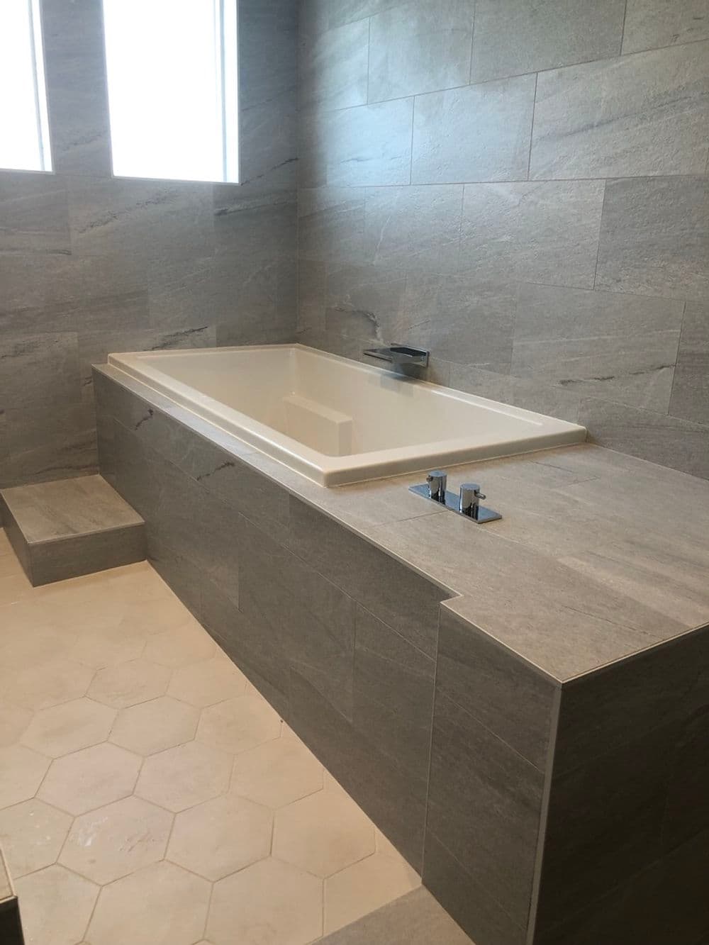 Modern bathroom featuring a spacious white bathtub with gray tiled walls and floor.