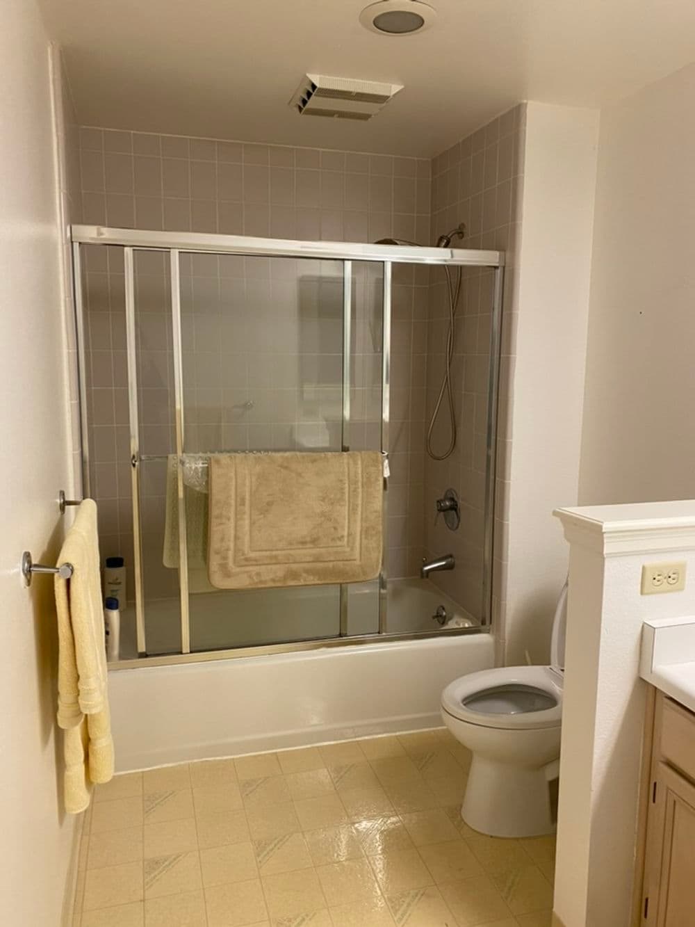 Modern bathroom with shower, tub, and toilet, featuring beige towels and tiles.