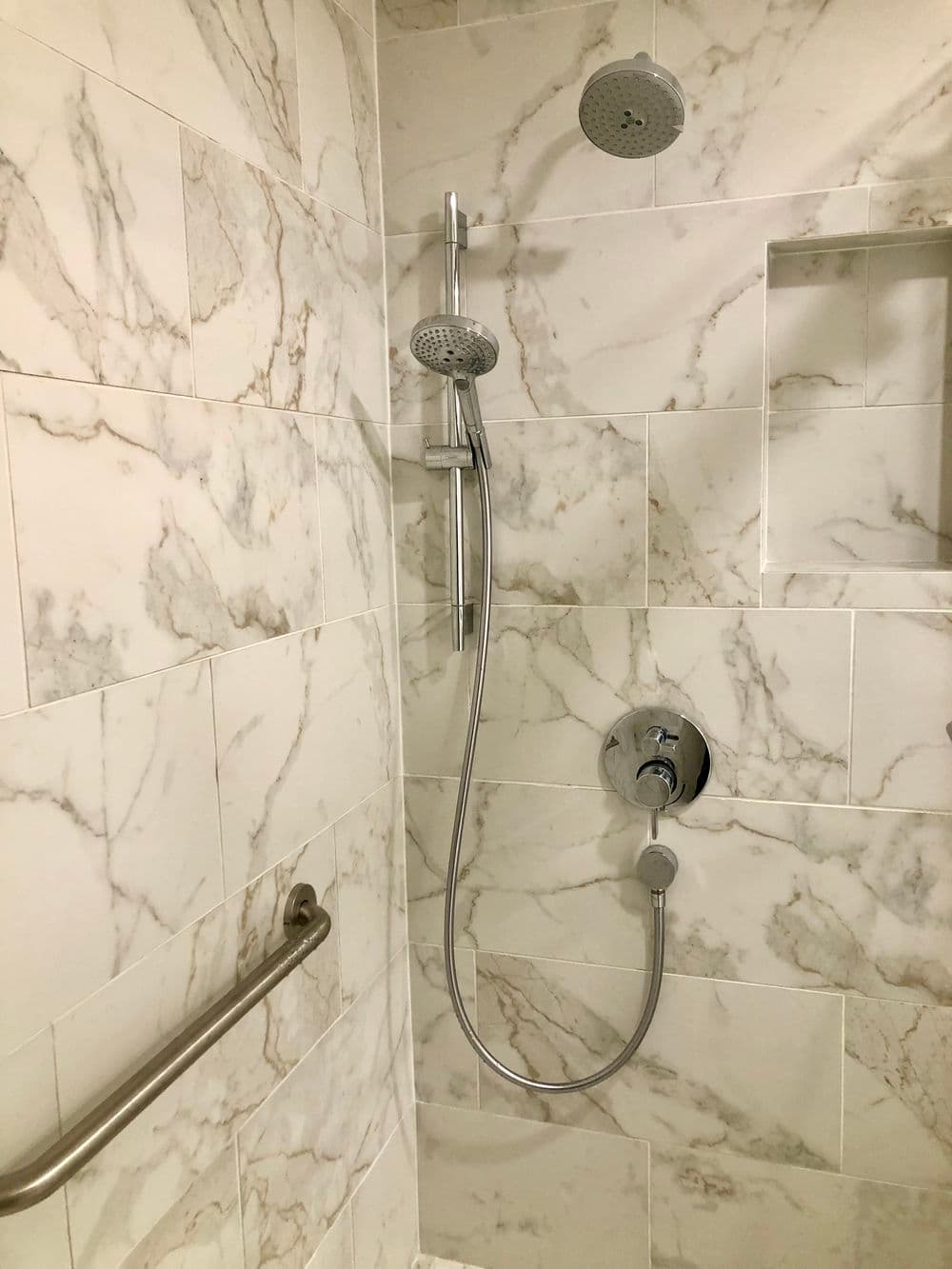 Modern shower with marble tiles, dual showerheads, and safety grab bar.