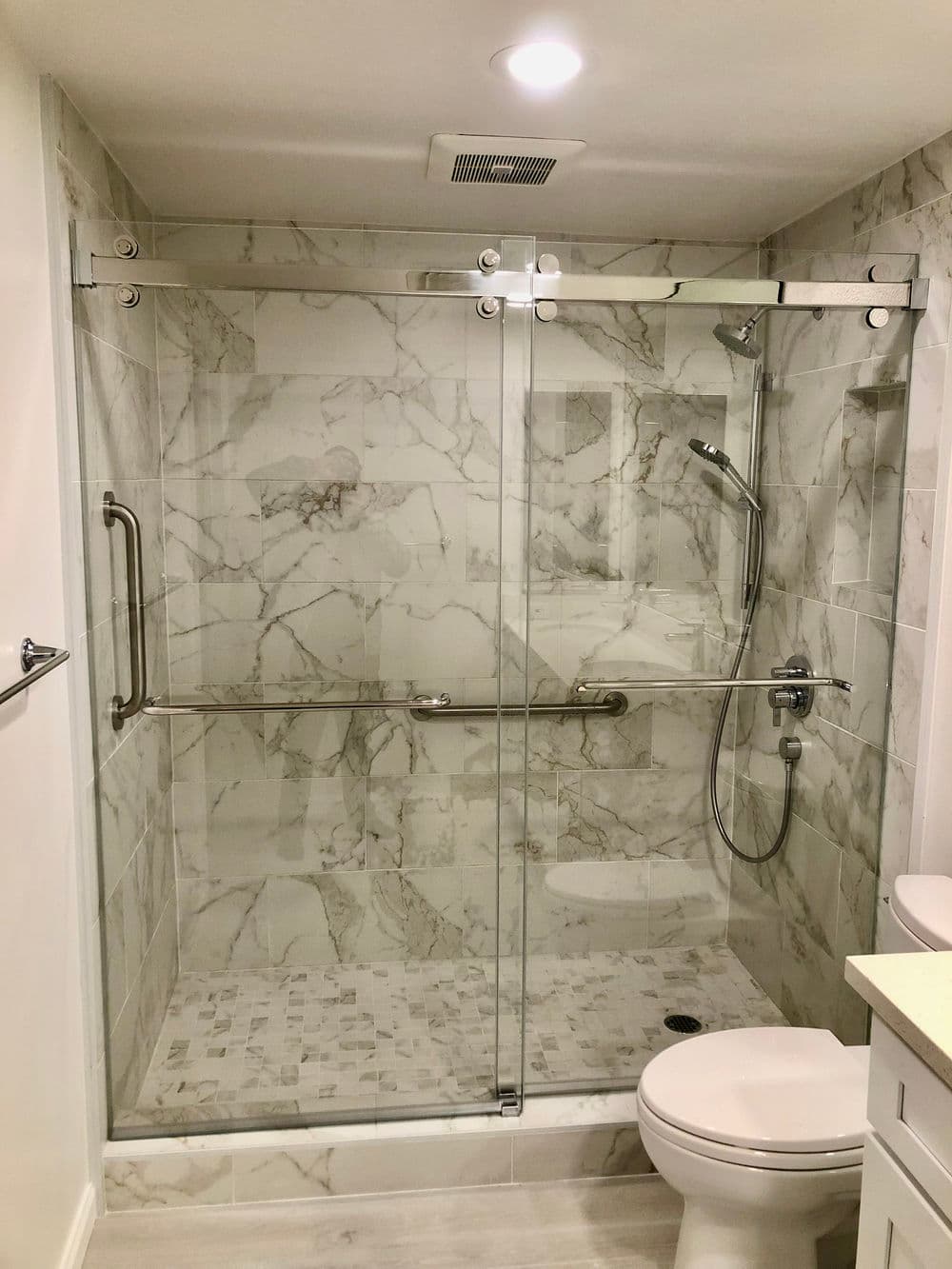 Glass shower enclosure with marble walls and a modern design, featuring polished fixtures.