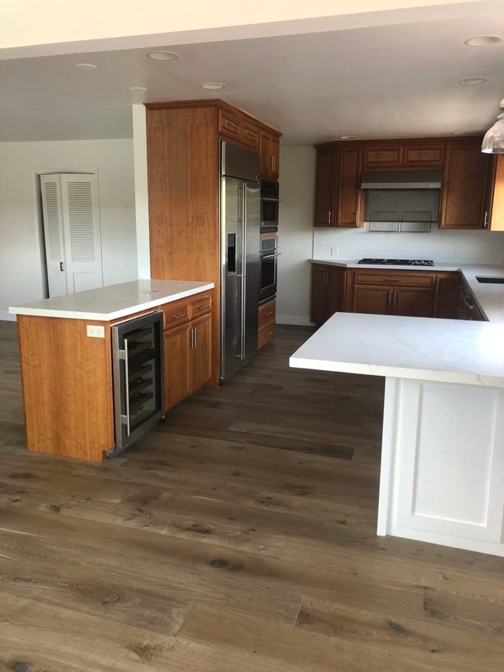 Modern kitchen with wooden cabinets, marble countertops, and hardwood flooring.