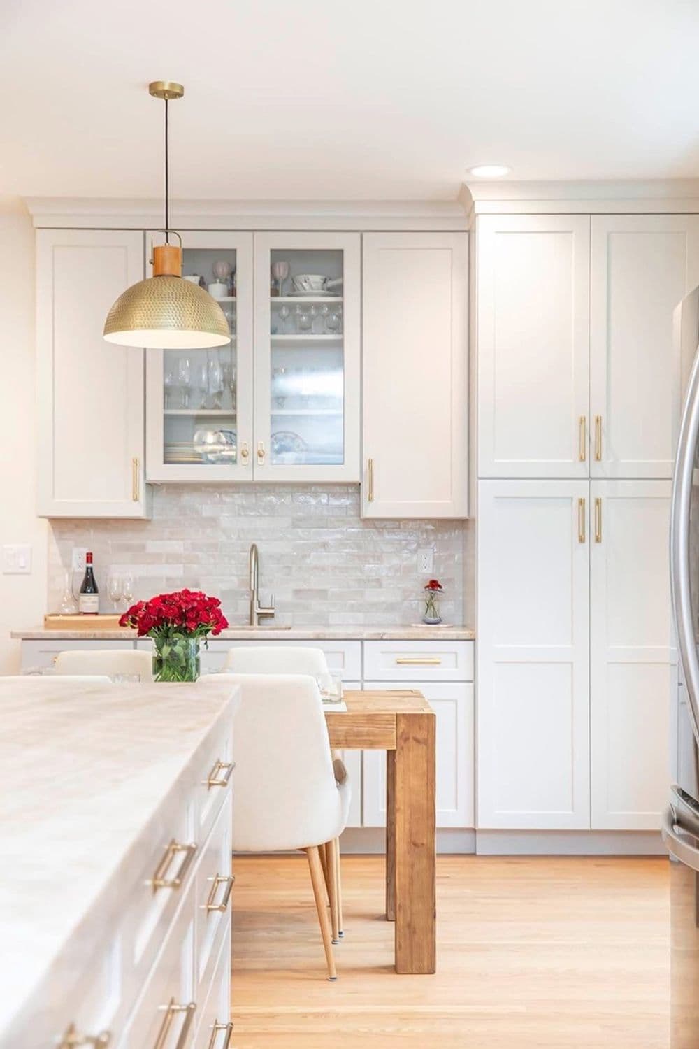 Modern kitchen with white cabinetry, wooden dining table, and stylish pendant lighting.