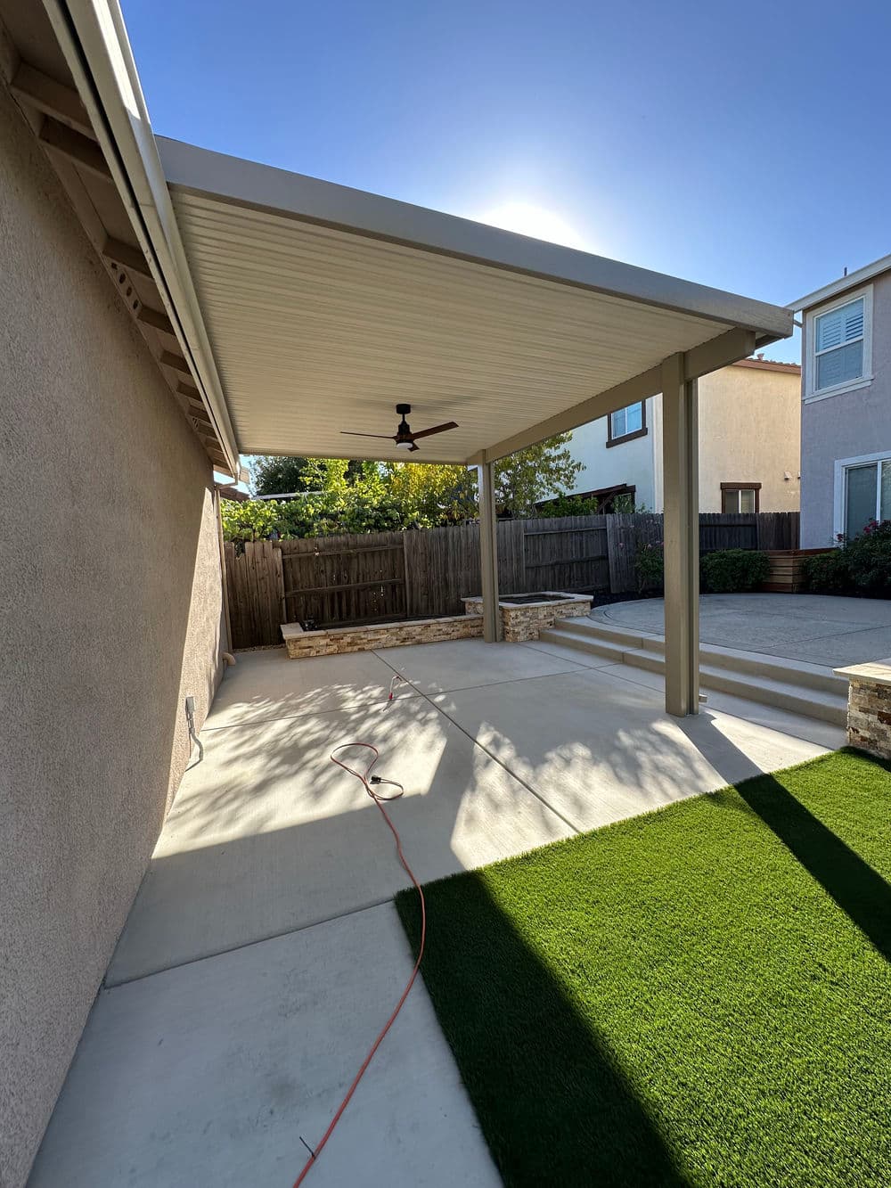 Covered patio with ceiling fan and landscaping, sunny backyard space for relaxation and gatherings.