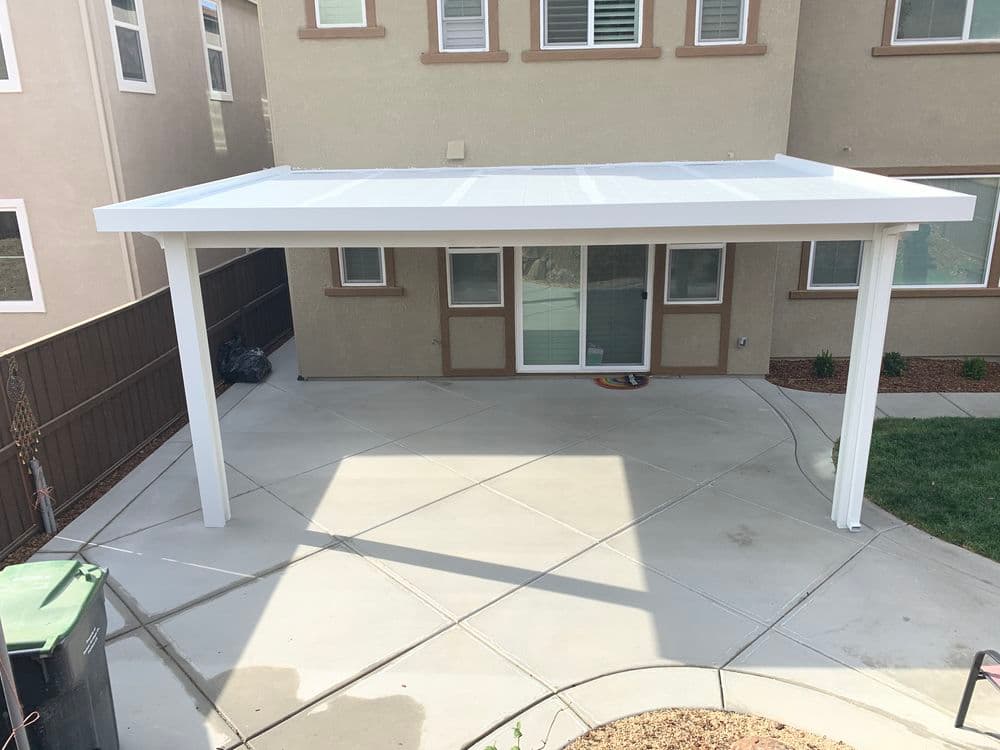 White patio cover over concrete backyard area with grass and trash bin nearby.