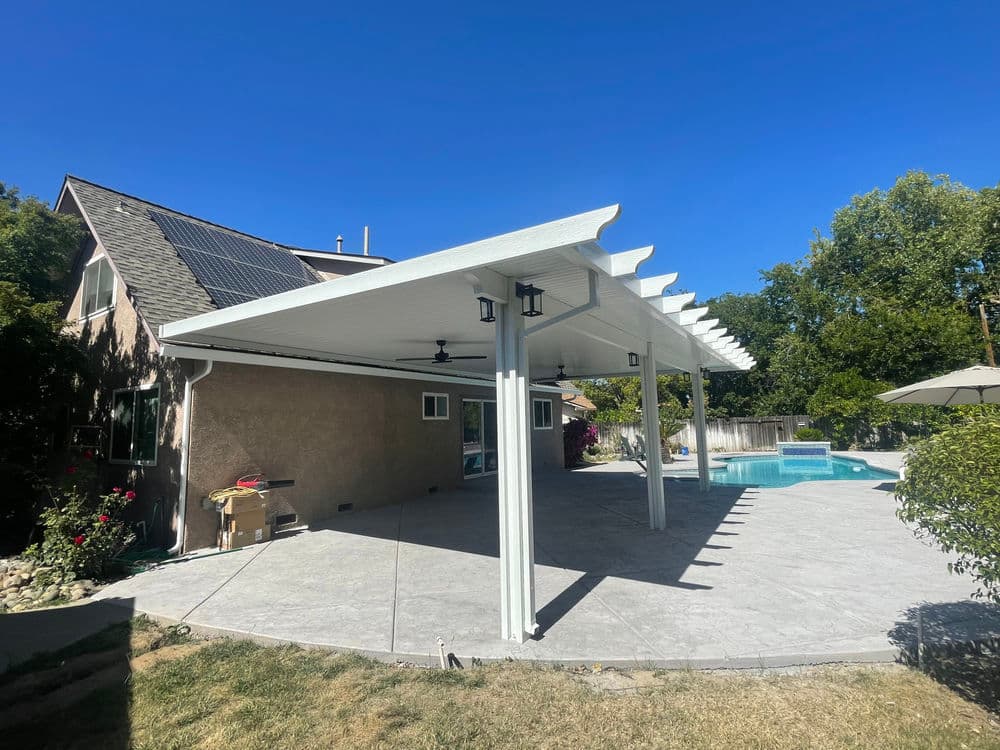 Modern outdoor patio with a pergola, pool, and solar panels on a house under a clear blue sky.