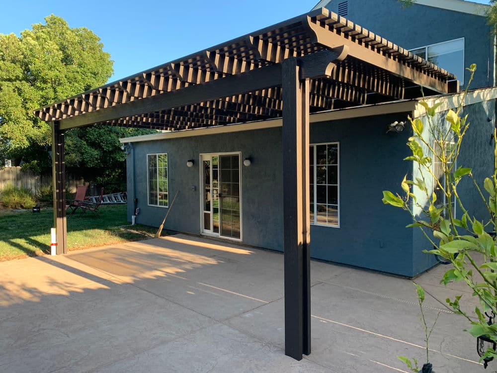 Modern outdoor pergola with a patio area, surrounded by greenery and residential home.