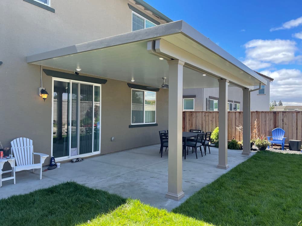 Backyard patio with a covered area, dining table, and seating beneath a blue sky.