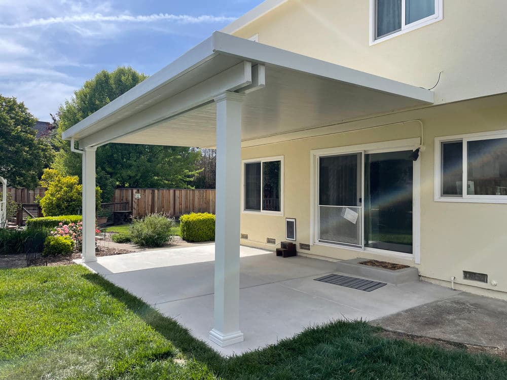 Modern backyard patio with a white canopy, concrete flooring, and lush green landscaping.