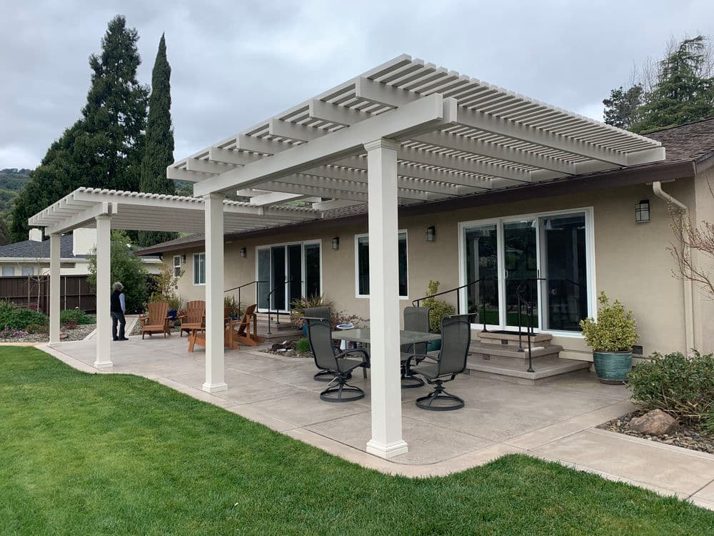 Modern patio with pergolas, seating areas, and landscaping beside a suburban home.
