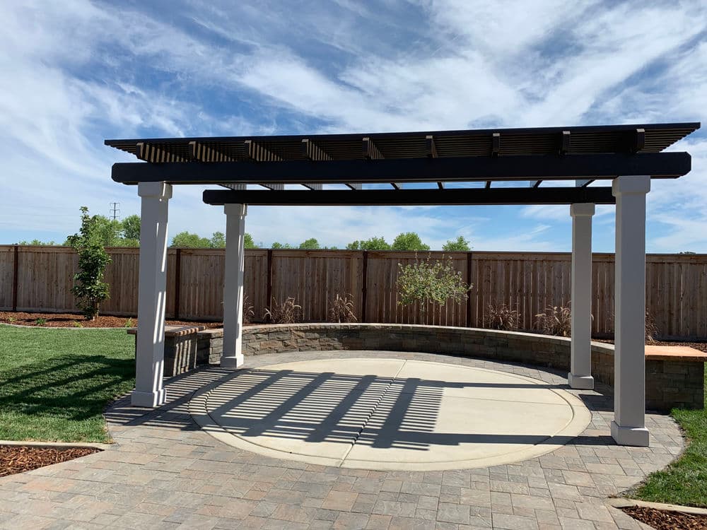 Modern backyard pergola with stone seating and landscaped garden under a blue sky.